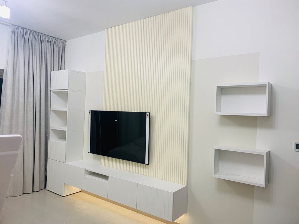 Wall-mounted television on a fluted panel with white open shelving and a low storage unit
