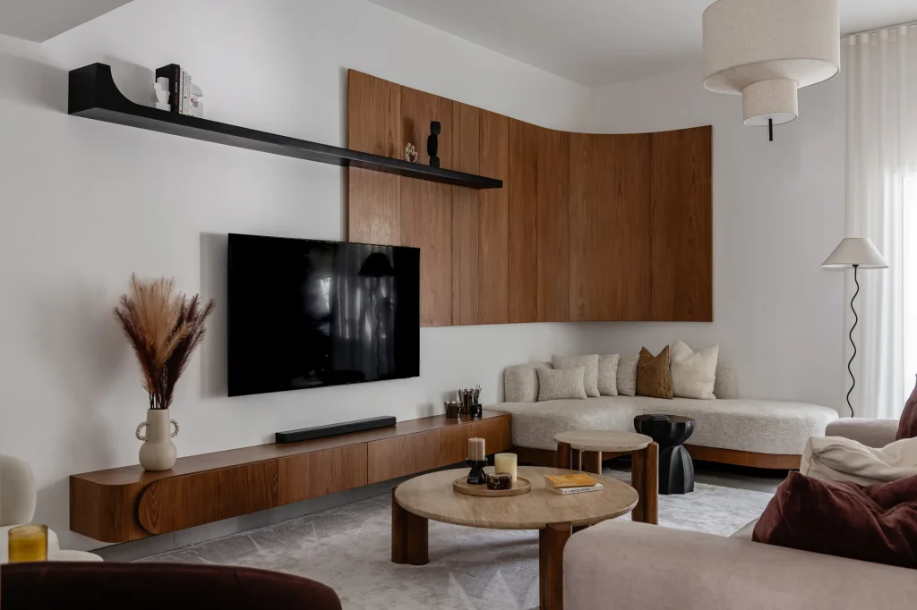 Projects We Have Done 15 Living room with a curved low cabinet, wood-toned wall panel, TV and black display shelf.